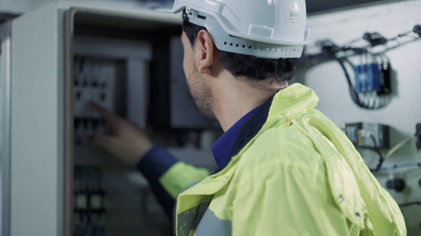 Engineer in hardhat and uniform checks the control board using chart in factory